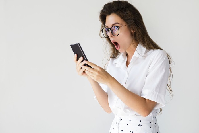 Young businesswoman with shocked face expression is using smartphone