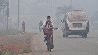 Seorang anak menutup hidung dengan menggunakan topi sekolah saat beraktivitas di luar ruangan yang masih diselimuti kabut asap.