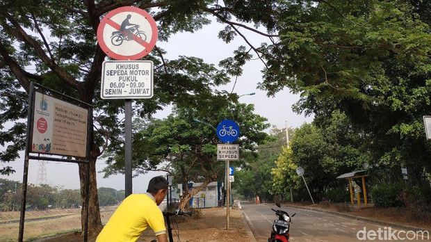 Seorang pesepeda sedang kerepotan mengangkat tunggangannya untuk melompati portal besi di jalur sepeda.