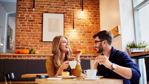 Couple of young people drinking coffee and eating cake in a stylish modern cafeteria