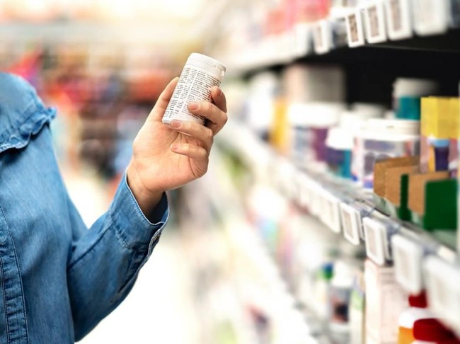 Customer in pharmacy holding medicine bottle. Woman reading the label text about medical information or side effects in drug store. Patient shopping pills for migraine or flu. Vitamin or zinc tablets.