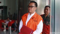 Imam tampak memakai baju tahanan dengan tangan diborgol dan membawa map merah.