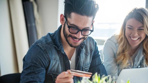 Front view of a stressed young couple facing financial problems, sitting on couch and looking at bills