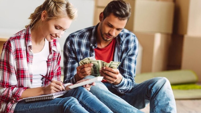 Front view of a stressed young couple facing financial problems, sitting on couch and looking at bills