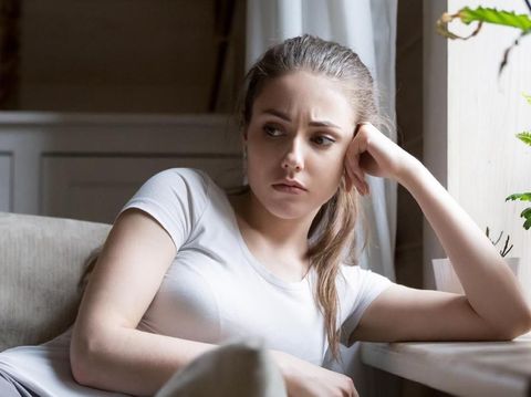 Frustrated thoughtful millennial woman sitting on cozy sofa at home. Beautiful young female having doubts, thinking about life, having problems, bored. Psychological therapy, personality crisis concept
