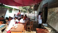 Tempat belajar itu dibuat di halaman rumah seorang warga, tak jauh dari sekolah mereka. Lantaran lahan yang terbatas, kelas terpal itu digunakan bergiliran. 