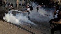 Dalam foto ini tampak demonstran menendang tabung gas air mata yang dilemparkan polisi di dekat stasiun kereta bawah tanah Santa Lucia saat aksi demo memprotes kenaikan harga tiket kereta dan bus di Santiago. (Foto: AP)