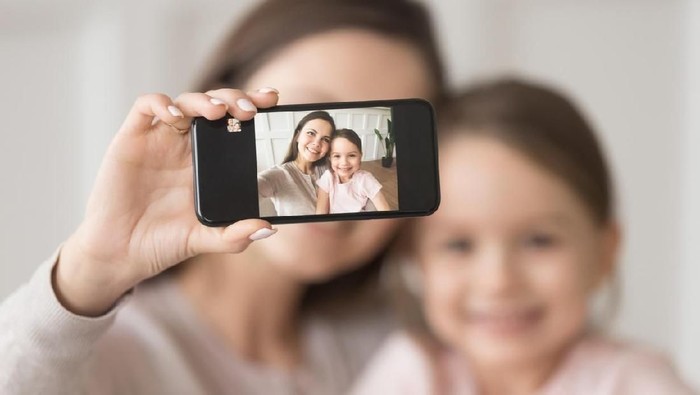 Happy mother laughing taking selfie with child daughter on smartphone at home, smiling single mom and cute girl playing making photo posing for self portrait, mommy and kid shooting instagram stories