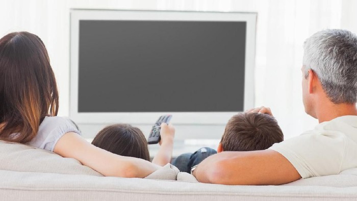 Family sitting on sofa watching television together at home