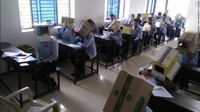 Salah satu staf sekolah mengambil foto para siswa yang duduk di deretan depan, yang semuanya memakai kardus di kepala mereka. Bagian depan kardus itu dilubangi agar para siswa bisa melihat meja dan soal ujian dengan jelas, namun tidak bisa melihat sekeliling mereka. Foto: Bhagat Pre-University College via CNN