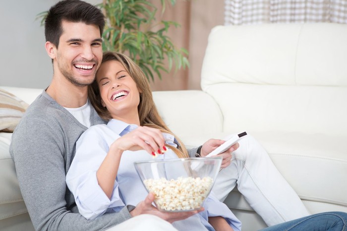 Couple watching TV, eating popcorn on a sofa at home