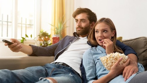 Couple watching TV, eating popcorn on a sofa at home