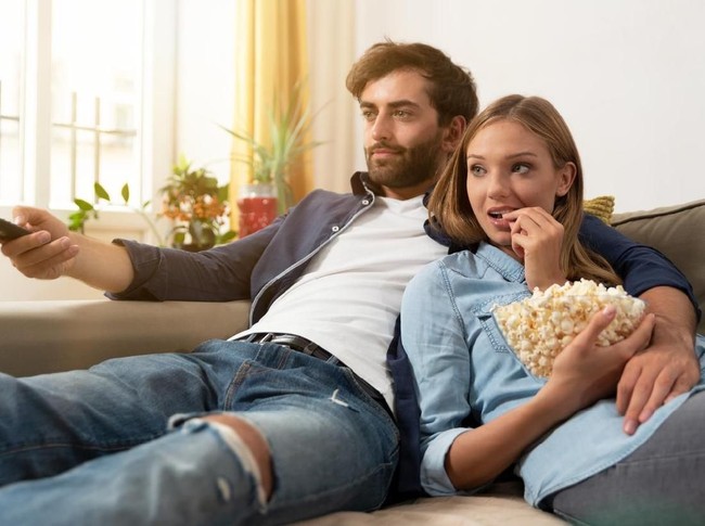 zodiak Couple watching TV, eating popcorn on a sofa at home