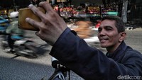 Seorang pengendara sepeda motor berhenti sejenak untuk berselfie dengan background karangan bunga.