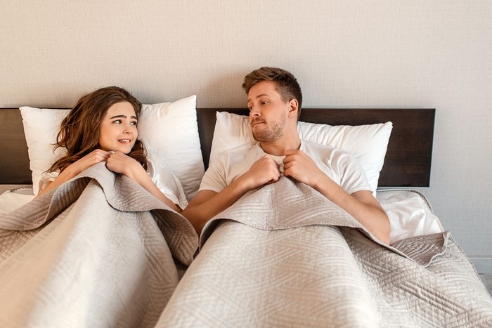 Young couple in the bed. Fear of sex, shy woman and man hidding under blanket before first intimacy