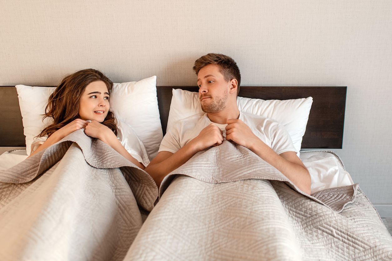 Young couple in the bed. Fear of sex, shy woman and man hidding under blanket before first intimacy
