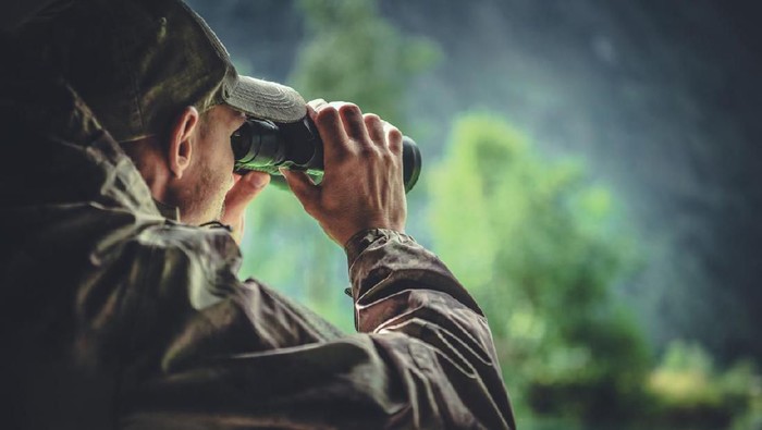 Caucasian Hunter in Masking Camouflage Uniform with Binoculars. Hunter Spotting Game. Poacher or Soldier Clothing.