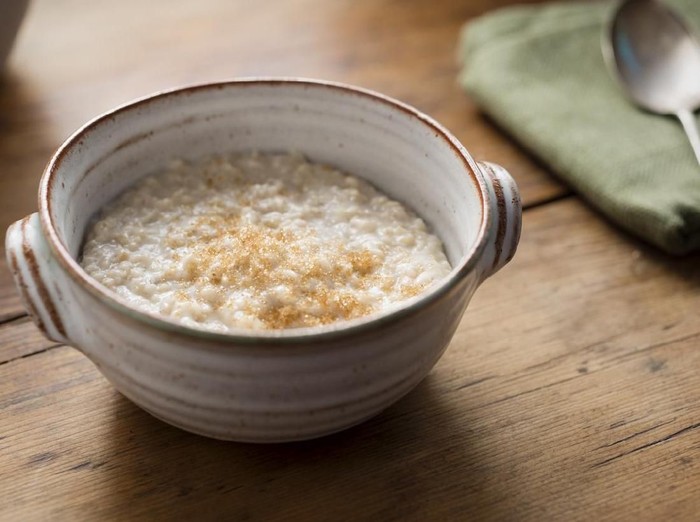 Photograph of a rustic hand made bowl filled with freshly made Porridge, topped with sprinkled Demerara sugar. Photographed on a rustic old pine rustic table.