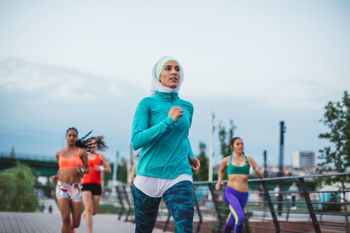 Multi ethnic group of young  women exercise outdoor, next to the river. They are wearing sport clothing, running, stretching, celebrate and support each other.