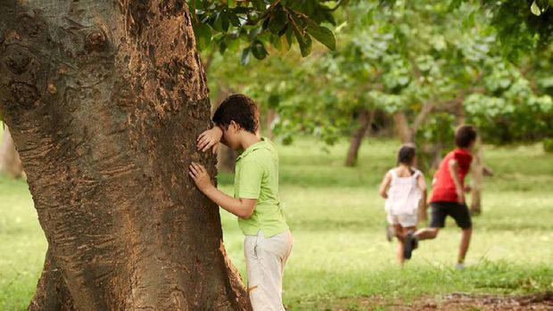 young boys and girls playing hide and seek in park, with kid counting leaning on tree