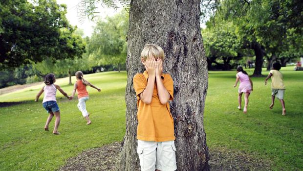 Boy (7-9) with hands covering eyes playing hide and seek in park, hiding from friends behind tree