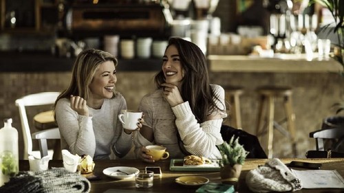 Young happy women talking and laughing while drinking coffee together in coffee shop.