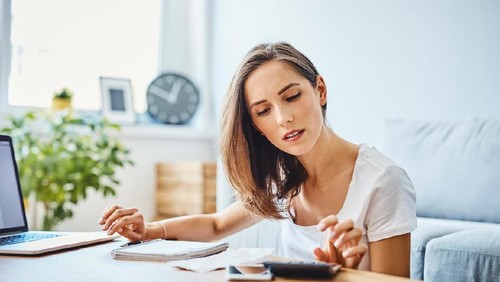 Young woman preparing home budget, using laptop and calculator
