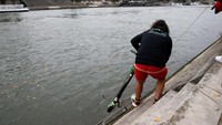 Untuk bisa menarik skuter, dia menggunakan tali yang ujungnya dipasang kait logam. Tak lama kemudian dia menarik tali yang sudah menyangkut di stang skuter dari air (Pascal Rossignol/Reuters)