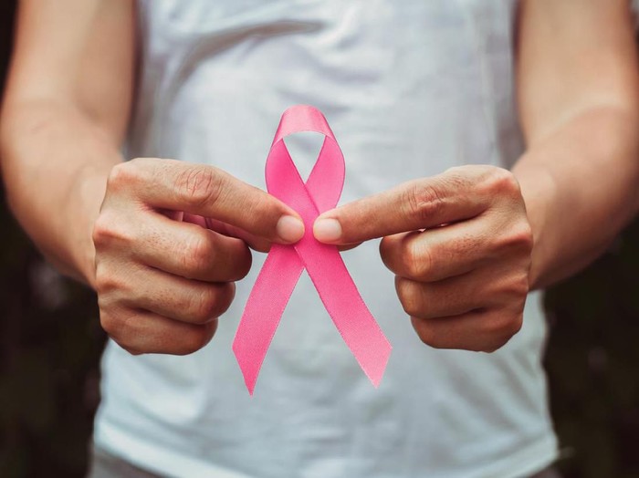 Kanker payudara Woman hand checking lumps on her breast for signs of breast cancer on gray background. Healthcare concept.
