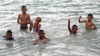 Tawa riang anak-anak menghiasi wajah mereka saat bermain air di laut.