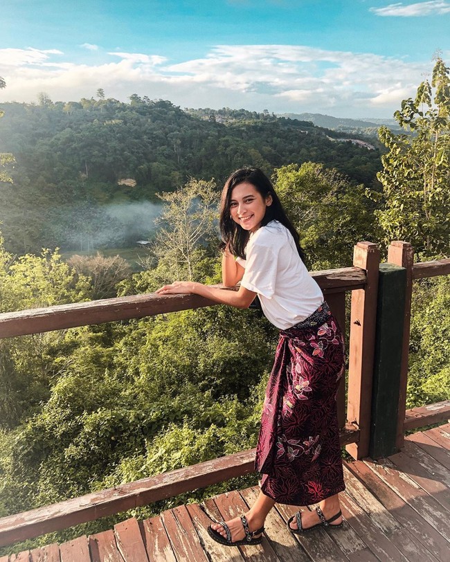 Indah tampak selalu bangga tampil dengan kain-kain tradisional. Saat berlibur dan menikmati pemandangan, Indah tampil kasual dengan kaus dan kain lilit batik.  Foto: dok. Instagram @indahpermatas