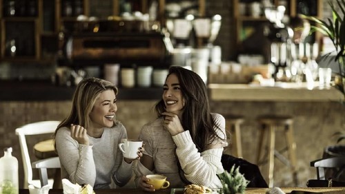 Young happy women talking and laughing while drinking coffee together in coffee shop.