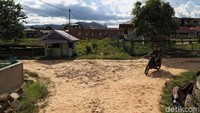 Pengendara sepeda motor melintas di jalan yang masih berupa tanah merah yang masih berada di sekitar kawasan pemukiman.