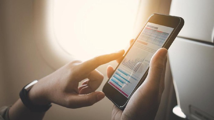Businesswoman on plane using smartphone with graph on screen.Business technology and travel concepts ideas