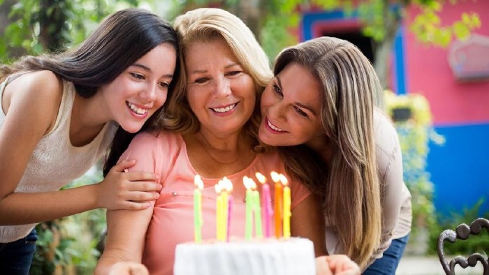 A grandmother celebrating her birthday with her granddaughter and daughter at her side in this horizontal shot.