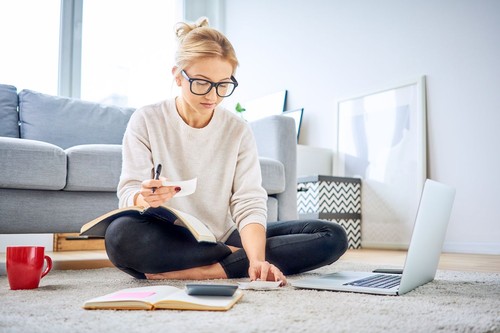 Young woman looking at bills while sitting on floor managing home budget