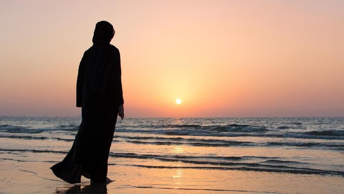Woman in hijab standing on the beach looking at horizon