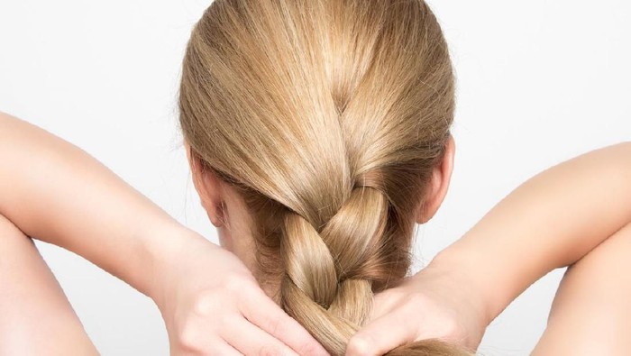 Gorgeous blonde woman braids her hair from behind