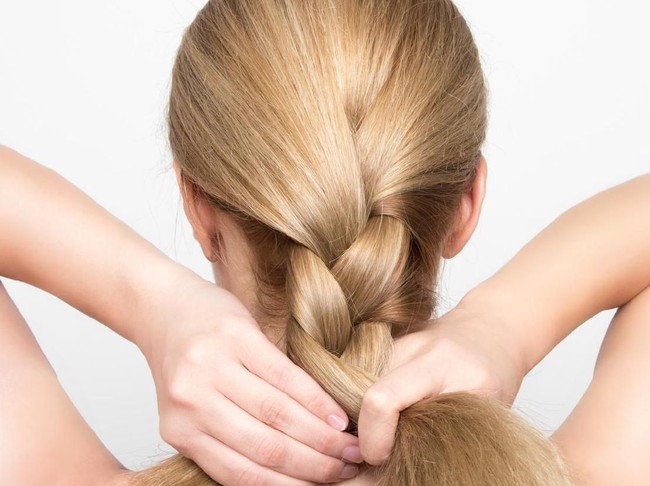 Gorgeous blonde woman braids her hair from behind