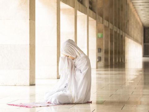 Young muslim woman praying in mosque while wearing prayer veil