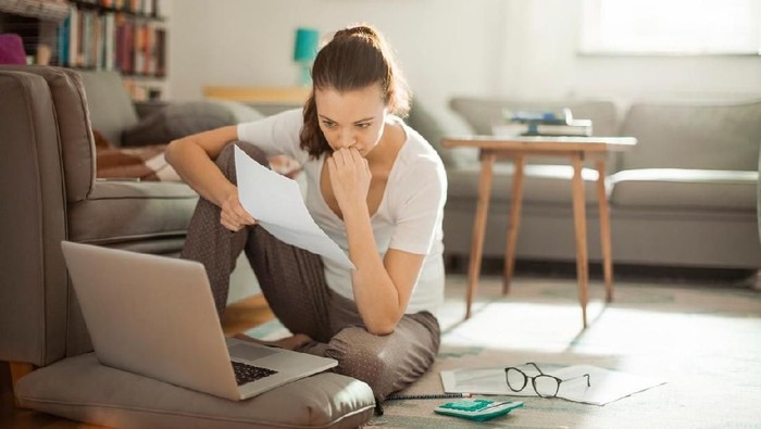 Young woman looking at bills while sitting on floor managing home budget