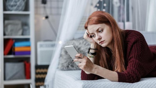 Worried, young teenager looking at the phone in her room