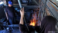 Sementara menantunya Tini (38) bertugas mengayunkan sepasang tongkat ububan agar angin keluar dan meniup bara api untuk memanaskan besi yang akan ditempa menjadi golok.