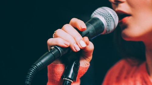 Singer at microphone. Woman singing and holding mic. Female vocal talent. Music show recital.