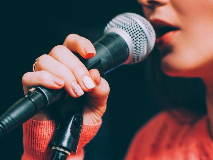 Singer at microphone. Woman singing and holding mic. Female vocal talent. Music show recital.