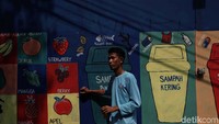 Seorang warga tengah membuat mural bertema buah-buahan.