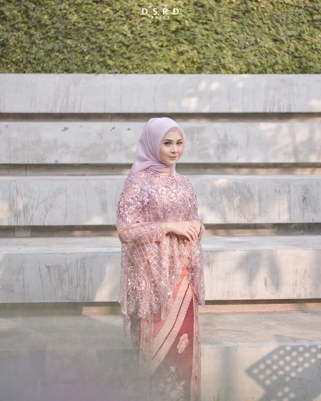 Kesha melengkapi hijabnya dengan kebaya model baju kurung warna pink dari brand Kilau Arti yang dipadukan kain lilit motif batik. Foto: instagram @dsrdbride