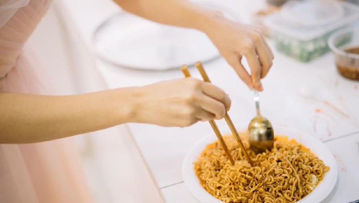 1147506630 Woman preparing instant noodle on plate in kitchen