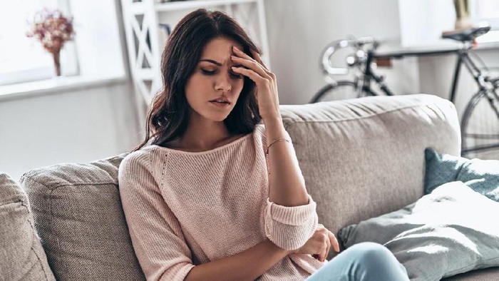 Frustrated young woman suffering from the headache while sitting on the sofa at home