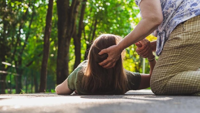Fainted girl helped by an old woman â€“ Teenager trying to get back on her feet while receiving support from an elder